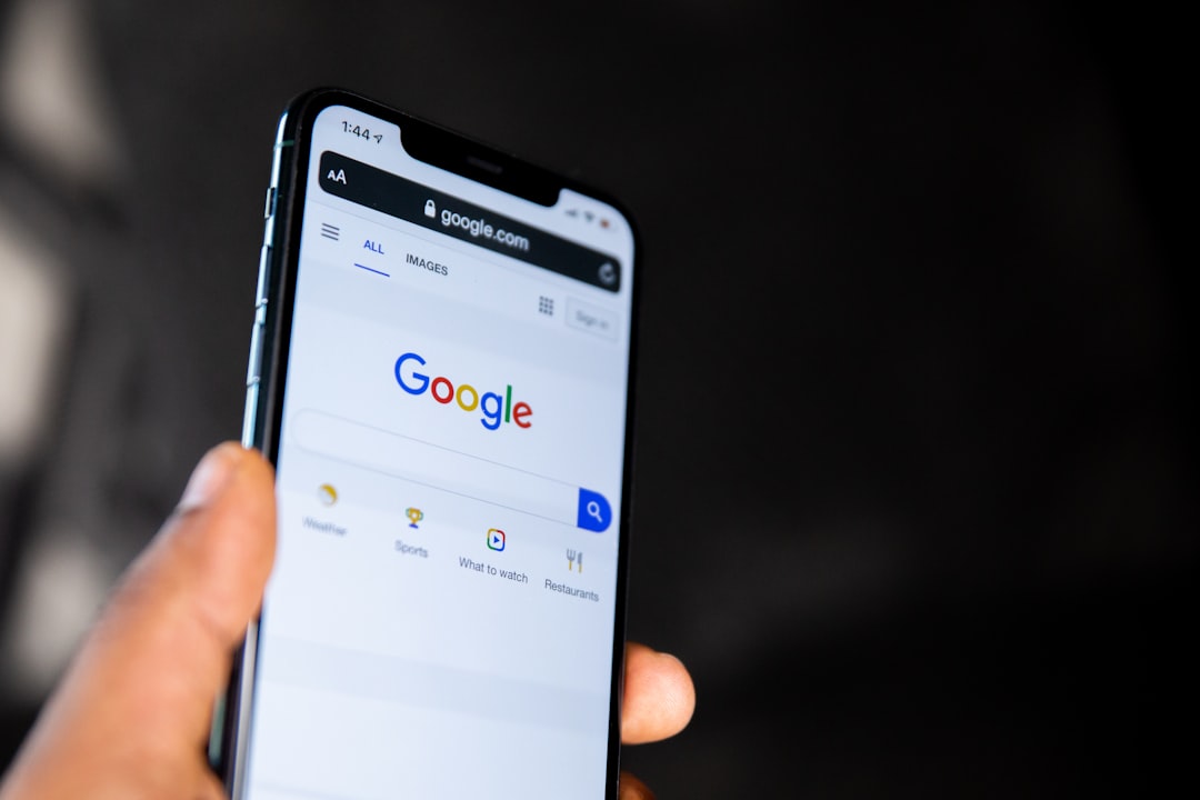A hand holding a smartphone displaying the Google search engine homepage